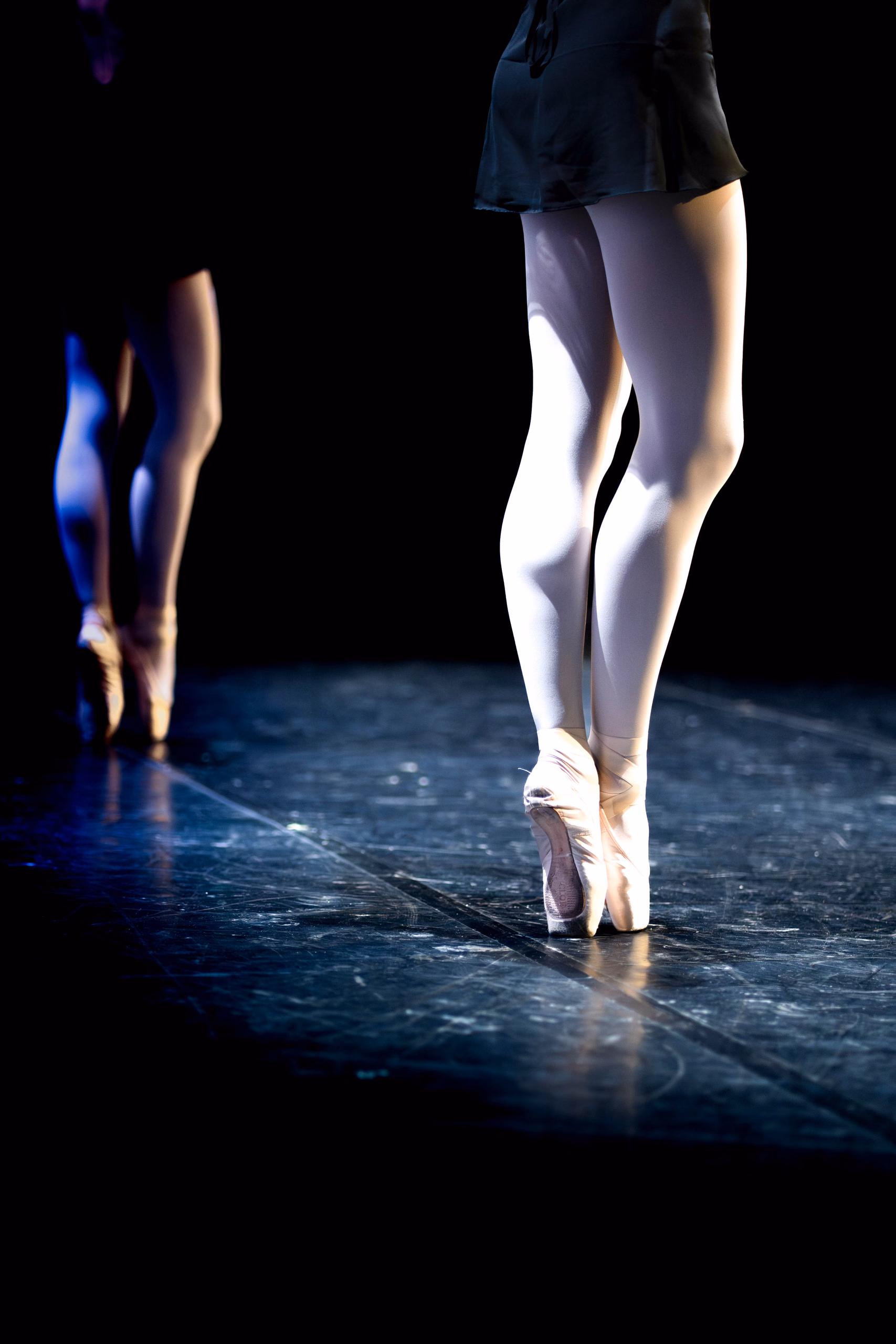 Gros plan sur des jambes en collants dressées sur pointes, sur un plancher de scène sombre
