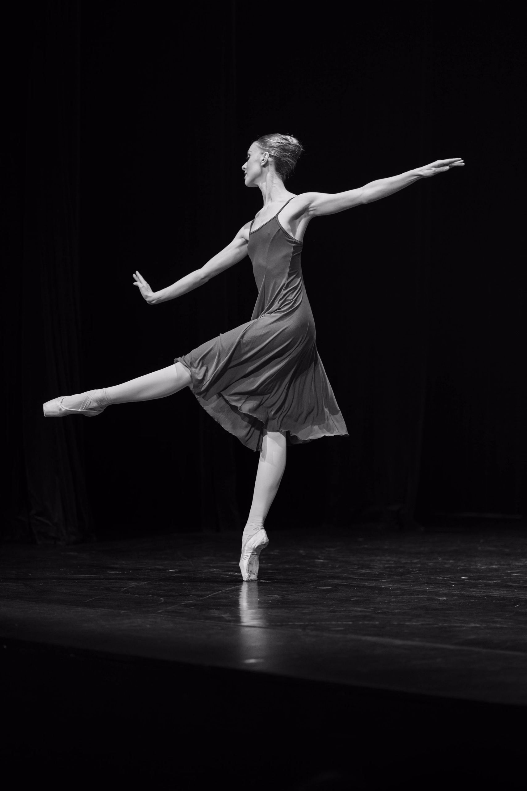Danse classique en noir et blanc : arabesque sur pointe en robe fluide, sur fond noir