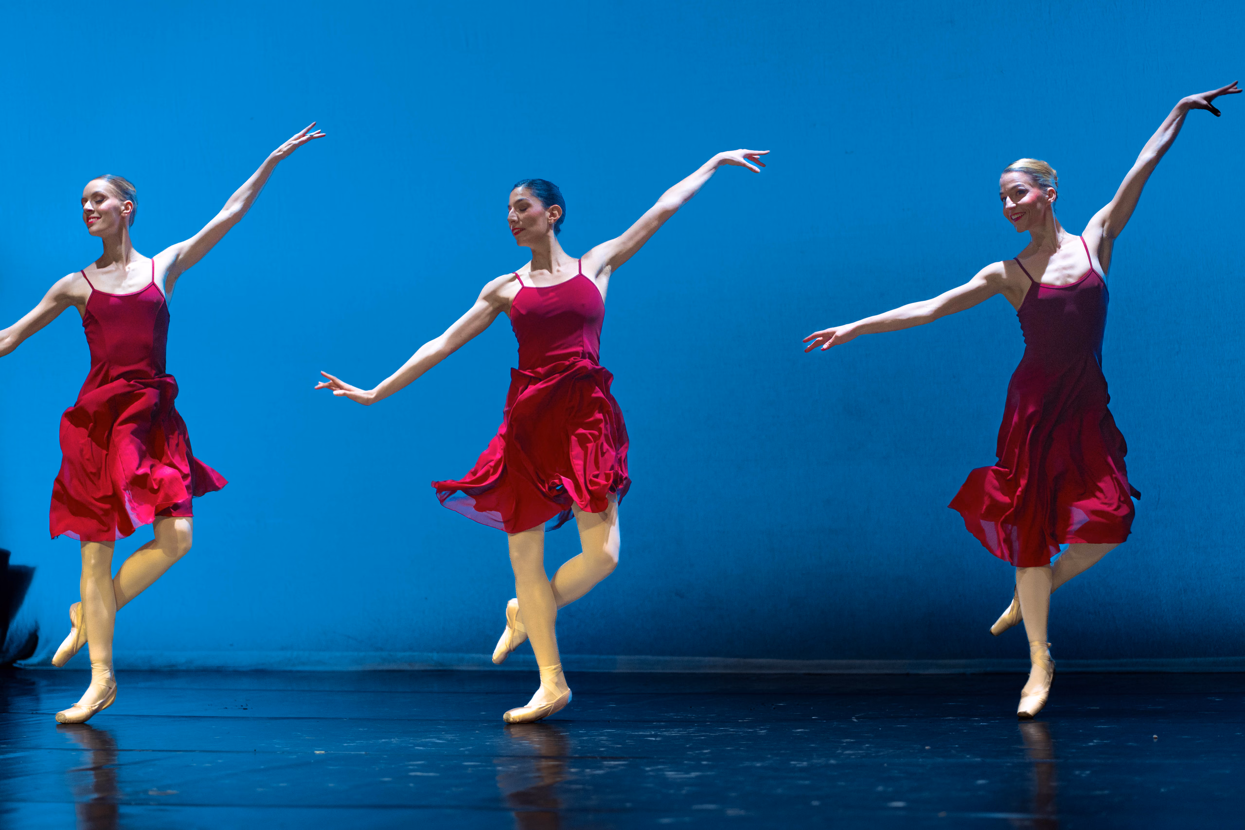 Trio de danse classique en robes rouges, bras levés, devant un fond bleu vif