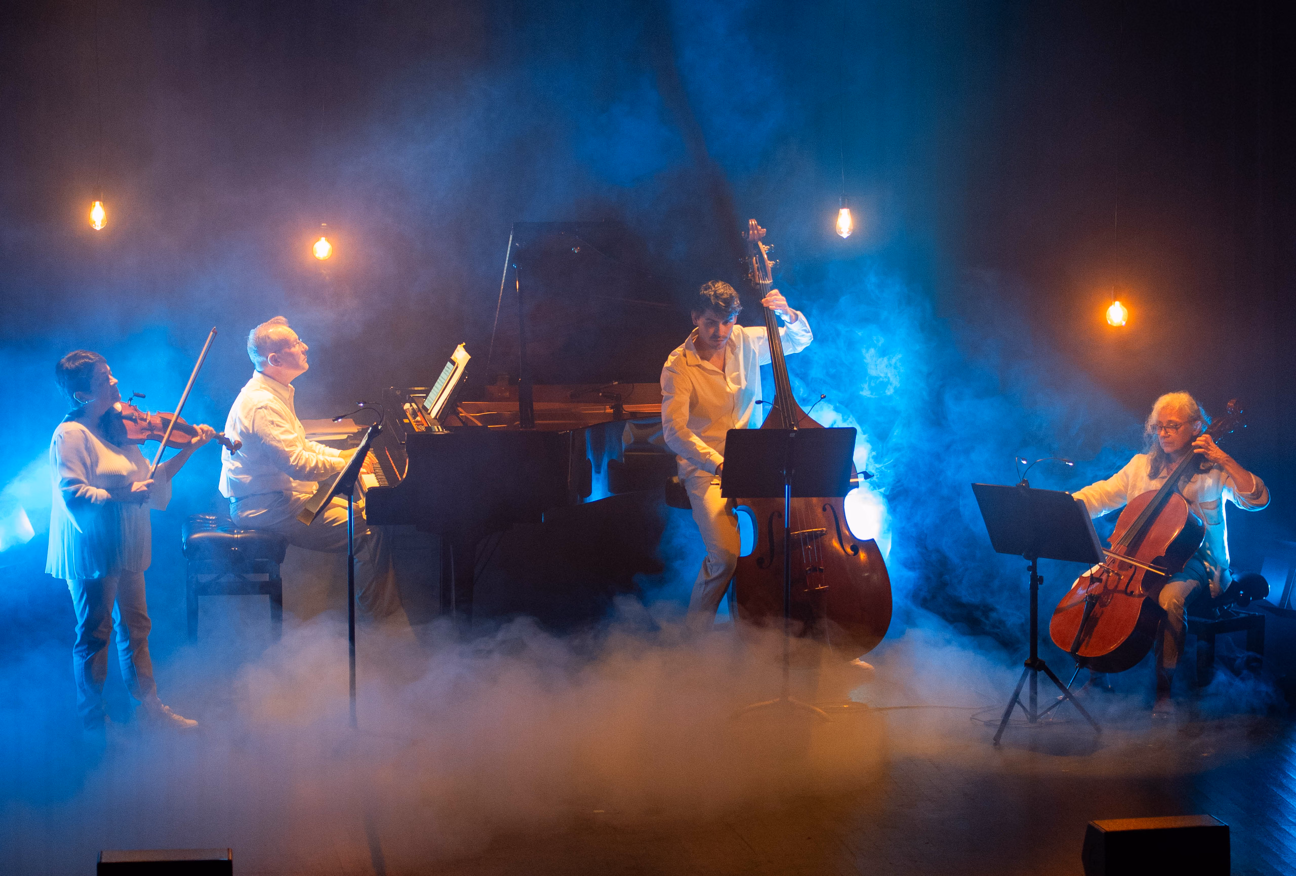 Quatuor vêtu de blanc (violon, piano, contrebasse, violoncelle) jouant dans la fumée sous une lumière bleue
