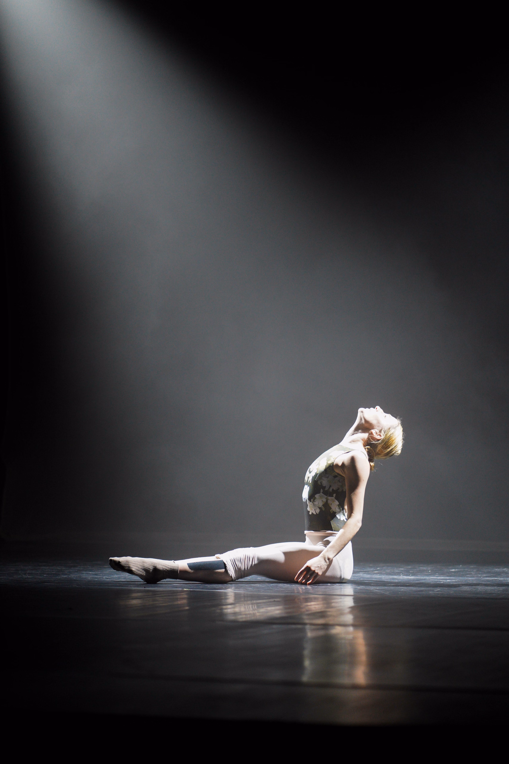 Danse contemporaine : au sol, tête renversée en arrière sous un faisceau de lumière dans la fumée